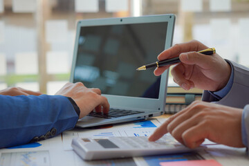 2 businessmen with pens to write data reports teamwork Discuss the up and down graphs on the financial side of the market economy on the table. with modern computer laptops