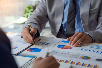 2 businessmen with pens to write data reports teamwork Discuss the up and down graphs on the financial side of the market economy on the table. with modern computer laptops