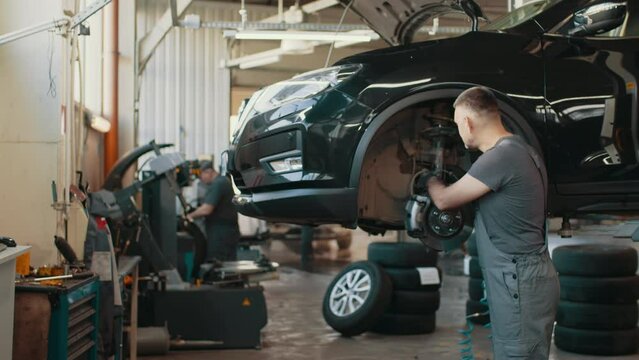 Portrait Shot of a Mechanic Working on a Vehicle in a Car Service. Modern Clean Workshop. Auto mechanic checking SUV suspension of a lifted car. Car service, repair, maintenance and people concept