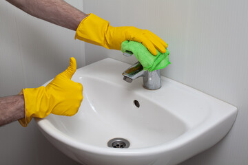 Man cleaning sink and faucet and showing thumb up. Housekeeping and hygiene concept