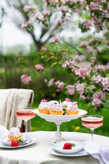 Festive spring romantic table setting with dessert in blossom garden. Vertical