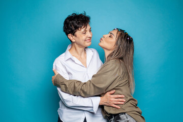 Beautiful family of mother and daughter together, hugging and kissing on blue studio background