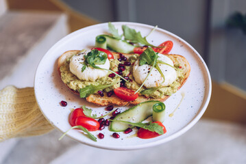 Waiter is hold a plate with poached eggs, avocado and cherry tomatoes on toast