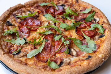 Close up salami pizza with mushrooms and arugula leaves.