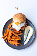 Tasty burger with fried egg served with fried sweet potatoes.