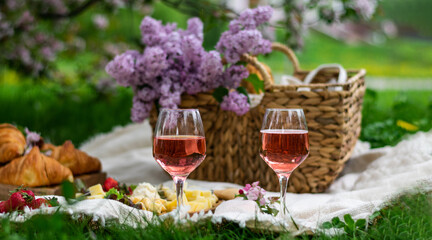 Closeup of two glass of rose wine , picnic basket, croissants, food and flowers on the grass. Banner