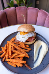 Tasty burger with fried egg served with fried sweet potatoes.