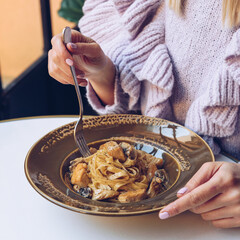 Woman is eating tagliatelle pasta in a restaurant