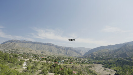 Fototapeta na wymiar A drone flying over the mountains.Action. Beautiful daytime summer landscape with mountains and blue sky overhead, also with residential buildings and green trees.