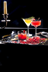 Red and yellow cocktails on a silver tray among carnival masks and rose petals