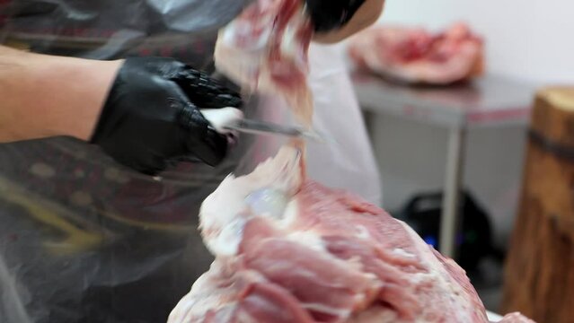 The professional butcher carves parts and bones from pork carcass with sharp knife at meat processing plant. Meat industry concept close-up 4K
