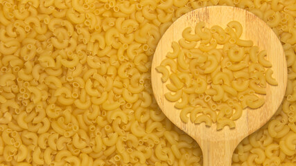 Yellow raw pasta on a wooden kitchen spatula. Against the background of pasta. Place for text.