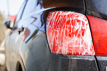 Broken red taillight of a black car wrapped with tape, close-up.