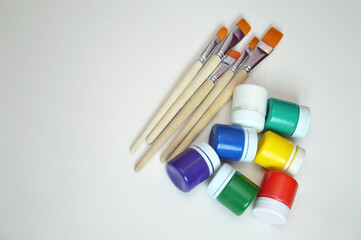 Jars of gouache paint in different colors and synthetic brushes. A set of objects for drawing....