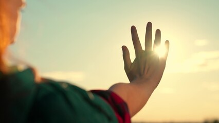 Naklejka na ściany i meble Happy teenage girl touches sun with her fingers. Hand of happy young woman plays with glare of sun. Girl holds out her hand at sunset. Sunrise between womans hands. Dreams of young woman traveler