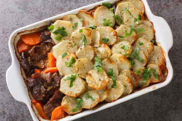 Homemade meat stew topped with sliced potatoes in ceramic bowl, traditional British pub food closeup in the baking dish on the table. Horizontal top view from above