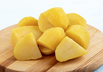 Peeled sliced boiled potatoes on a wooden cutting board.
