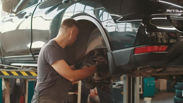 Selective focus disc brake on car, Car brake repairing in garage. Portrait Shot of a Mechanic Working on a Vehicle in a Car Service. Modern Clean Workshop. Car service, maintenance and people concept