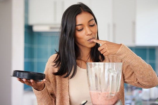 It tastes as yummy as it looks. Shot of a young woman preparing a healthy smoothie at home.