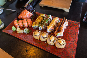 Verschiedenes Sushi mit verschiedenen Maki-Rollen und Nigiri-Rollen bestehnd aus verschiedenem Gemüse, rohem Fisch, Reis und Seetang, serviert auf einer roten Servierplatte in einem Sushi Restaurant