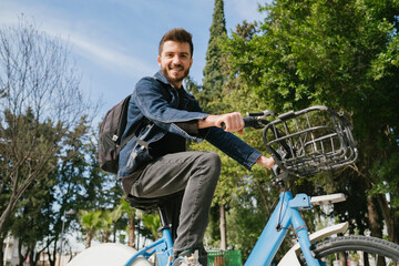 Cycling trip, handsome college student with a backpack prefers a bicycle as a means of transportation to school, green transportation method and green environment