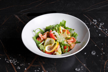 Salad with shrimps, vegetables and herbs in a white plate on a black background