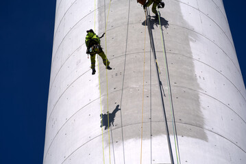 Two industrial climbers roping from chimney and cleaning graffiti vandalism with special equipment on a sunny spring day. Photo taken April 6th, 2022, Zurich, Switzerland.