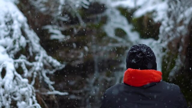 Rear view of an Indian man standing in front of the Jana waterfall during the snowfall near Kullu in Himachal Pradesh, India. Man stands in front of waterfall during snow storm. Man enjoying snowfall.