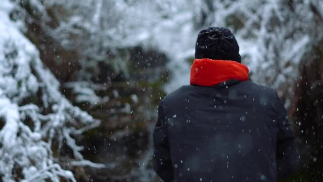 Rear view of an Indian man standing in front of the Jana waterfall during the snowfall near Kullu in Himachal Pradesh, India. Man stands in front of waterfall during snow storm. Man enjoying snowfall.