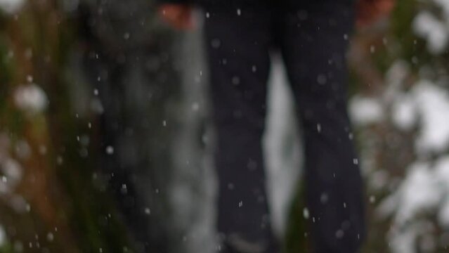 Closeup slow motion shot of snowfall with legs of a man standing in front of Jana waterfall in the background at Kullu in Himachal Pradesh, India