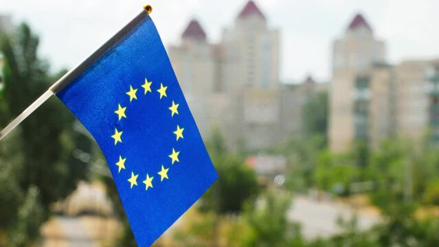 Flag of the European Union set against blue sky and city street. Europe flag waving. Circle of gold Stars on the blue European flag. The holiday flag of the EU on the sun. Copy space for text
