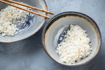 Bowls with steamed white rice on a grey concrete background, horizontal shot