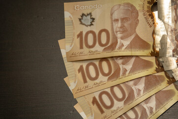 Close up of brown Canadian hundred (100) dollar bills with black backround and copy space.