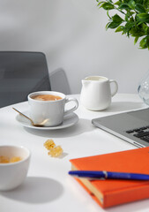 cup of coffee jar of milk laptop and notebook on the white table 