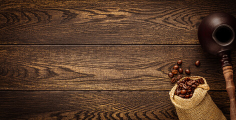 Burlap sack with organic coffee beans and turkish cezve pot over wooden background. Cropped image...
