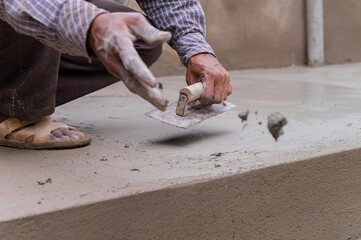 Indian labour levelling plastered floor using flat trowel and cement manually, Stock image.