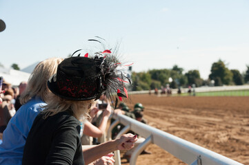 Woman watching horse race at race track with big fancy hat - obrazy, fototapety, plakaty
