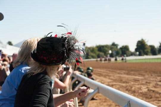 Woman watching horse race at race track with big fancy hat