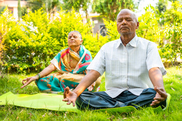 Senior couple on yoga mat meditating during morning at park with closed eyes - concpet of relaxation, healthy lifestyle and self care