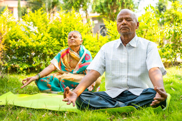 Senior couple on yoga mat meditating during morning at park with closed eyes - concpet of...