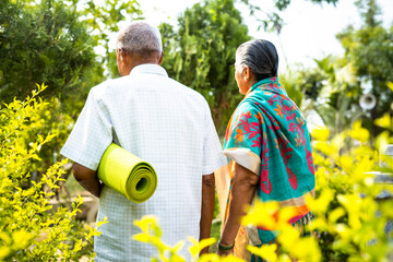 focus on yoga mat, back view shot of elderly couple with yoga mat going for exercise at park...