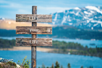 live your life text quote written on wooden signpost outdoors in nature with lake and mountain...