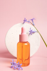 Serum glass bottle with pipette and beautiful flower on pink background. Natural Organic Spa Cosmetic concept. Front view.