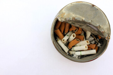 Lots of dirty used cigarette butts in an ashtray on a white background. Health, smoking, harm to...