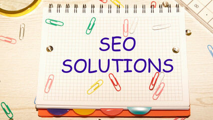 seo solutions text on a notebook in a cage with scattered paper clips on a notebook and a table