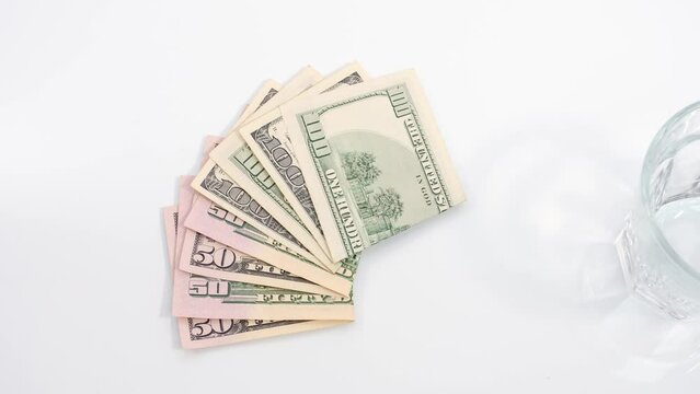 Folding fifty and one hundred dollar bills and a glass filled with colorful capsules, pills and drugs. Payment for treatment, purchase of pharmaceutical products, spending on medicines.