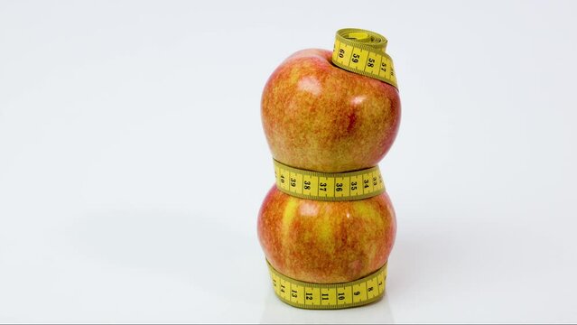 Two ripe red apples wrapped in yellow measuring tape. The concept of healthy food, weight loss, diet. Stop motion animation.