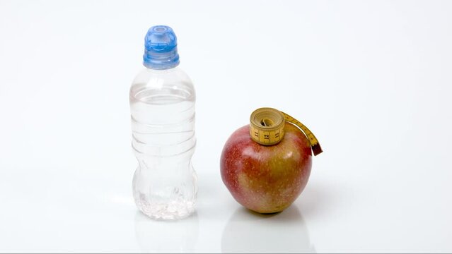 A yellow measuring tape moves from a bottle of water to a ripe red apple. The concept of healthy food, weight loss, diet. Stop motion animation.