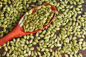 Pumpkin seeds in a wooden spoon on a wooden background. Healthy food. Scattered seeds of pumpkin. Flat lay