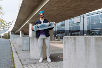 Young smiling skater holding longboard. Happy Caucasian man wearing casual clothes